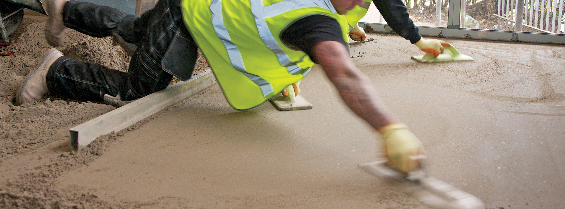 Screed being levelled out by two workers both in high vis jackets